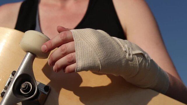 Young woman holding a skateboard, demonstrating a bandaged wrist after a fall or injury. Concept of sports injury, resilience, extreme sports and first aid for sprains. Girl with a skateboard. Sports 