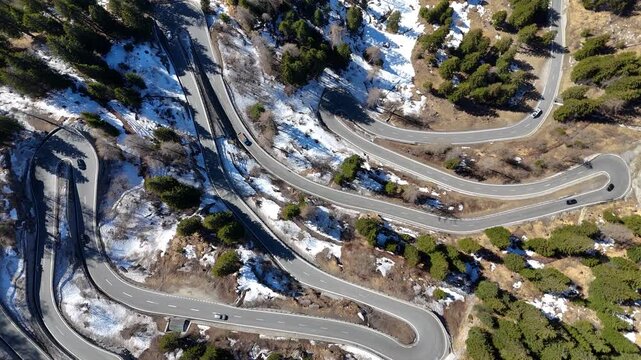 stacked hairpin loops wind down mountainside cars truck cross switchback bends sparse pine snow patches maloja pass overhead aerial drone footage graubunden switzerland