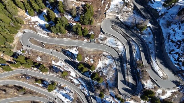 switchback loops curve past rock tunnel portal forested slope car crosses hairpin bends patchy snow maloja pass drone footage aerial graubunden switzerland val bregaglia
