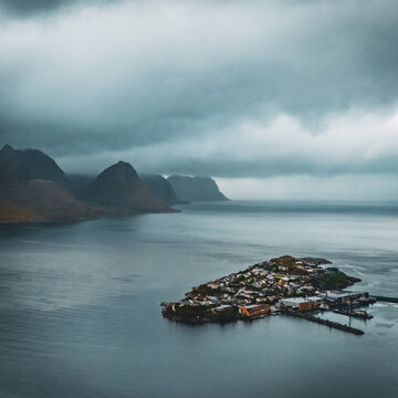 Dramatic aerial view of island village husoy surrounded by northern fjord and mountains under stormy cloudy sky with copy space