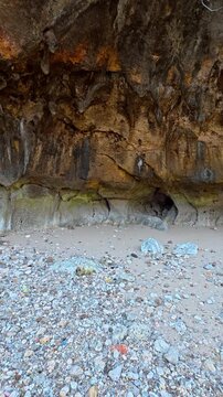 Pebble beach beneath rugged coastal cave and weathered rock cliff