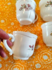 Hand holding vintage white porcelain teacup on bright yellow cloth