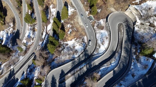 stacked switchback hairpin loops birds eye view multiple vehicles van winding mountain road guardrail retaining wall forest patches malojaschlange maloja pass graubunden switzerland alps