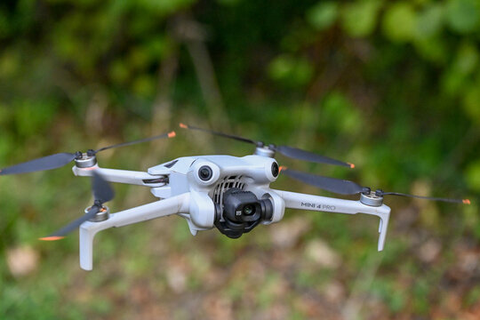 drone de loisirs en vol sur un fond de v&eacute;g&eacute;tation et de verdure. Mod&egrave;le DJI mini 4 pro avec cam&eacute;ra et nacelle, les 4 h&eacute;lices tournent au bout des bras pliables.