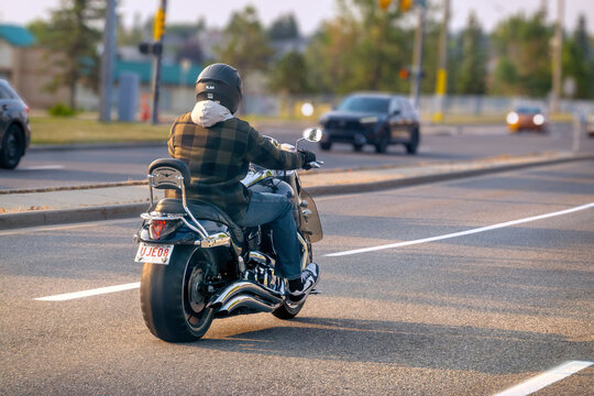 Calgary, Alberta, Canada. September 18, 2026. A rear view of a person riding a cruiser motorcycle down a city street in daylight.
