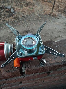 Portable camping gas stove with blue flame burning on a brick surface outdoors