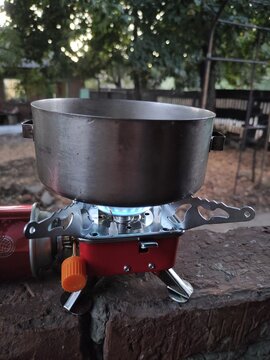 Portable camping gas stove with metal pot heating on a brick wall outdoors