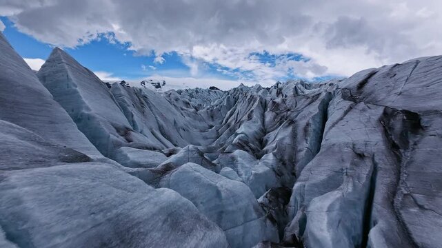Dynamic FPV drone flight skimming above and between deep glacier crevasses on glacier, Iceland. Cinematic aerial footage revealing blue ice formations and dramatic glacial landscape.