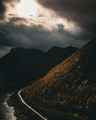 Aerial view of a winding coastal road along a colorful autumn mountain slope and fjord under dramatic sky with copy space © Quality by Simon