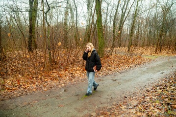 Fototapeta premium Young Woman Walking Along a Forest Path Talking on Smartphone During Autumn