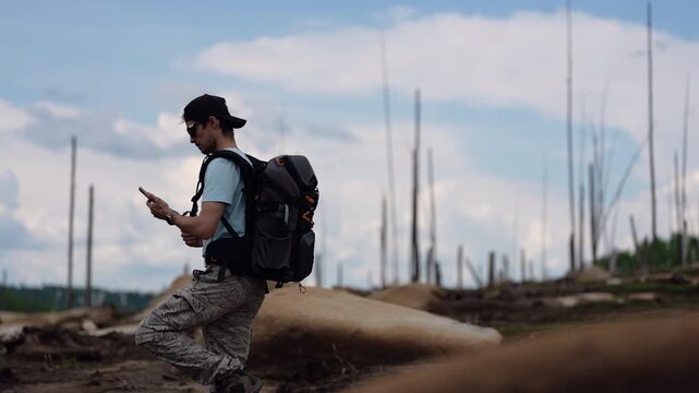 Traveler with backpack checking smartphone in wild open landscape, enjoying calm freedom and exploration