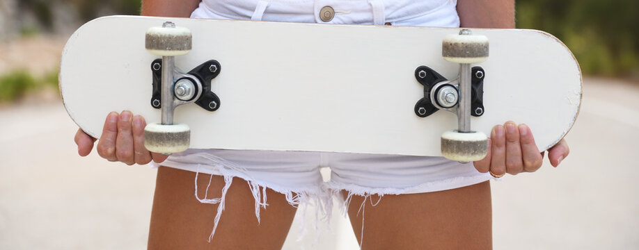 Girl in denim shorts holding white skateboard close up.
