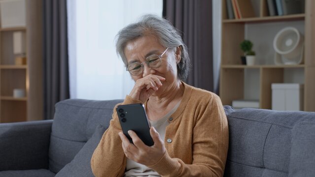 Emotional senior Asian woman reacts while looking at her smartphone at home, suggesting a touching online message, digital communication, personal connection and meaningful moments in later life.