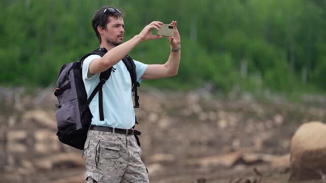 Traveler with backpack photographing wild nature using smartphone, enjoying peaceful freedom and open exploration
