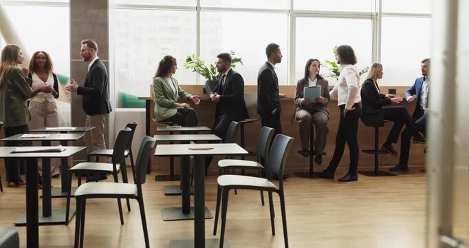 Business professionals networking during office meeting discussion. Groups of colleagues converse across a lounge with tables and stools near windows. Concept of teamwork and collaboration.