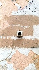 A vertical close-up shot of a small electronic doorbell button mounted on a heavily weathered, textured wall with peeling layers of white and beige paint, with a thin wire extending downward across th © Natali