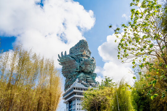 BALI, INDONESIA &ndash; OCTOBER 19, 2024: Gigantic GWK statue on pedestal framed by golden trees under blue sky in Bali park.