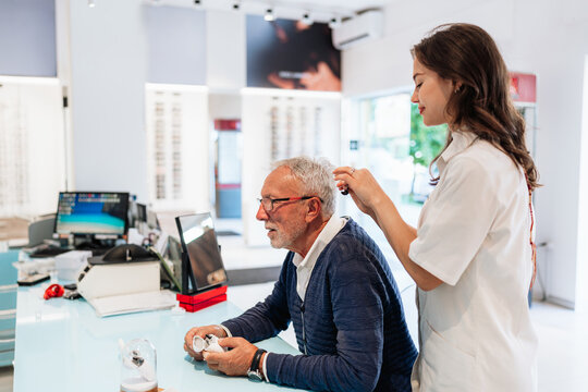 Medical specialist adjusting a sound amplification device for an elderly man during a professional consultation in a modern healthcare facility, focusing on wellness and hearing health.