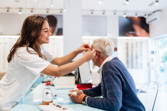 Medical specialist adjusting a sound amplification device for an elderly man during a professional consultation in a modern healthcare facility, focusing on wellness and hearing health.