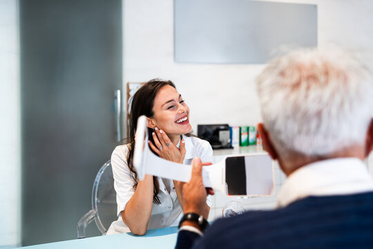 Professional hearing care professional showing modern acoustic devices to an elderly patient in a bright medical clinic consulting room.