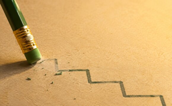 Pencil erasing a line on a grid paper graph, leaving behind smudges. The eraser works on an imperfect curve, changing its path. This image represents correcting errors or changing business strategies