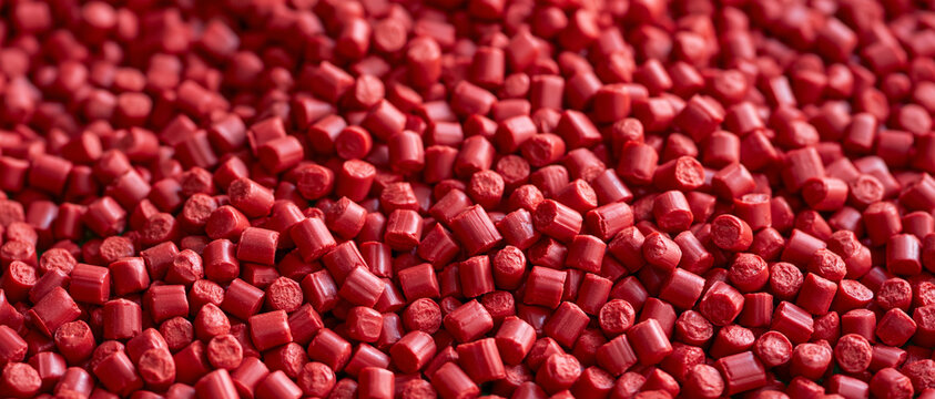 Vibrant red plastic granules and polymer resin pellets in a high-angle full frame close-up, illustrating the essential raw materials used across diverse industrial manufacturing processes
