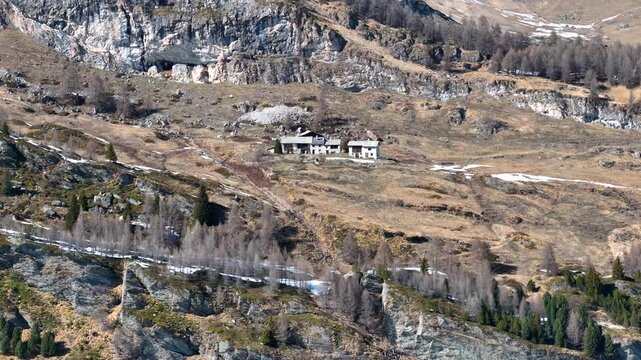 stone alpine farmhouses cluster remote hillside meadow engadin valley switzerland larch forest slope rocky cliff snow patches isolated hamlet drone orbit aerial shot