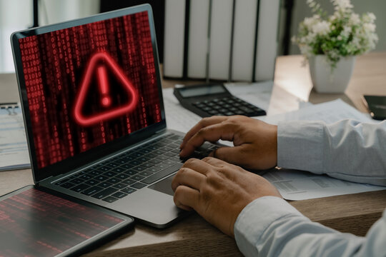 Businessman using laptop with red cybersecurity warning and digital code, showing malware attack, virus infection, computer security alert and cyber risk awareness.