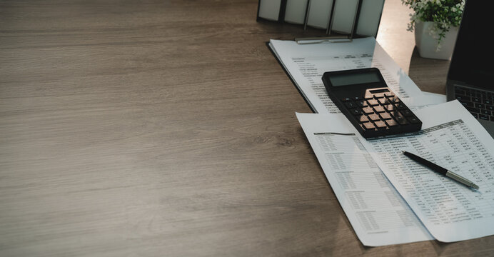 Financial accounting workspace with calculator, printed reports and laptop beside wide copy space, showing finance review, bookkeeping and business reporting.