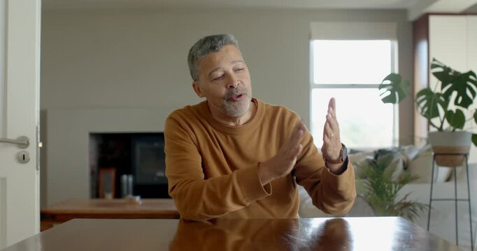 Senior man in brown sweater sitting at table, gesturing with hands, expressing enthusiasm