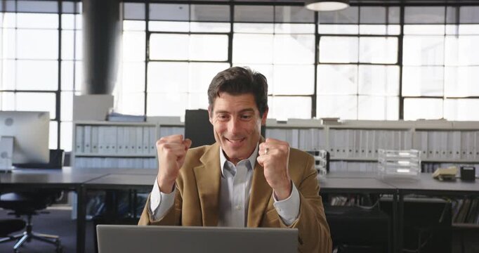 Businessman celebrating success at office desk with laptop, feeling accomplished