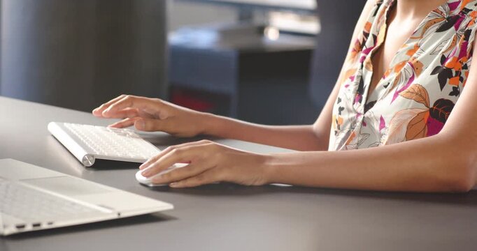 Hands typing on wireless keyboard at modern office desk with laptop nearby