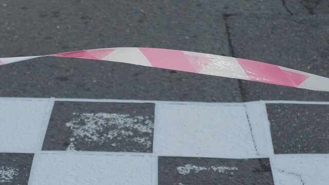 Red and white striped barrier tape swaying in the wind above a black and white checkered traffic calming speed bump on an asphalt street