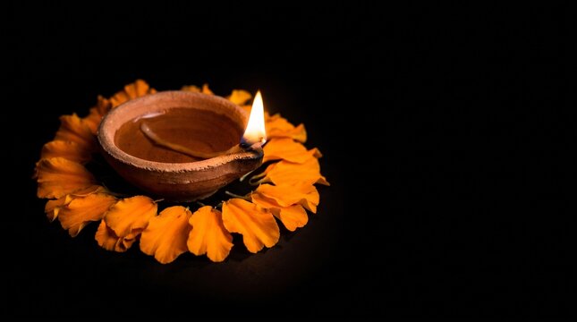 Single lit clay diya with marigold petals on black copy space