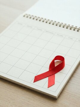 A red ribbon placed on a calendar page representing World AIDS Day awareness and health advocacy. Healthcare campaign symbol for HIV testing, prevention, and support in a professional setting.