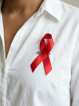 A red ribbon pinned to a white shirt collar as a symbol for World AIDS Day. Raising global awareness and supporting healthcare research. Inspiring solidarity and empathy for patients.