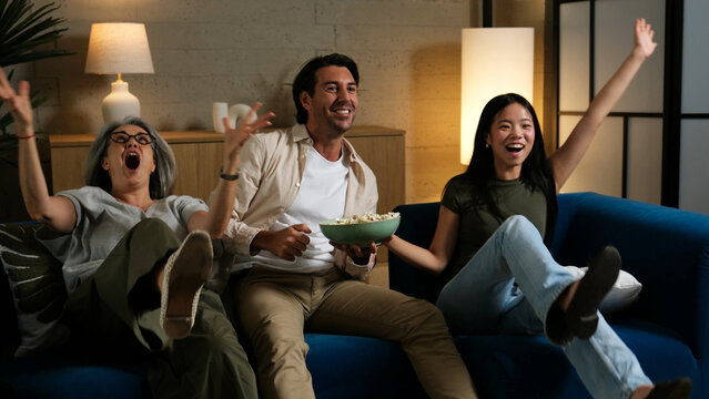 Happy family watching TV together, celebrating a win with popcorn