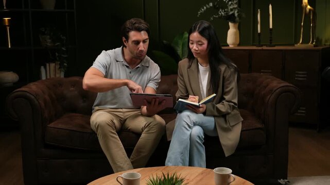 Journalist taking notes while interviewing a man with a tablet for a podcast or television program