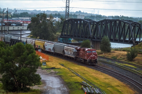 Calgary, Alberta, Canada. September 18, 2026. A freight train traveling past a steel truss railway bridge during daylight.