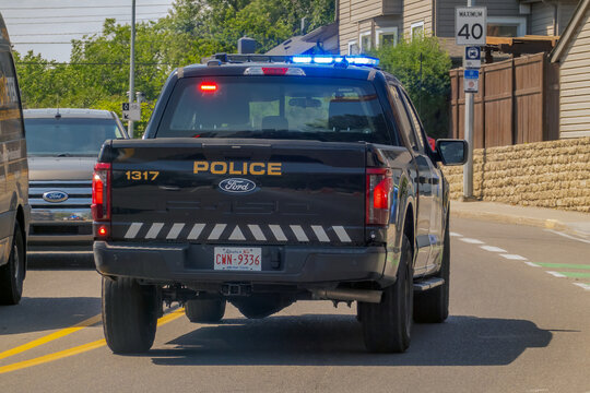 Calgary, Alberta, Canada. September 18, 2026. A rear view of a black police pickup truck driving down a suburban street with active lights.