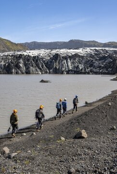Tourists with ice axes and helmets on the lakeshore of a glacier lagoon, glacier tongue with crevasses and lake, S&oacute;lheimaj&ouml;kull, South Iceland, Iceland