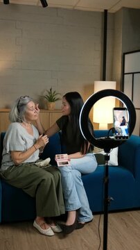 Young Asian woman and her senior grandmother filming a beauty tutorial for social media at home
