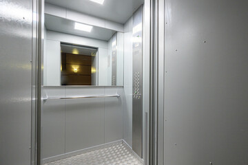 Elevator lobby features metallic walls, textured floor, horizontal handrail, mirrored panel, recessed ceiling lights, stainless steel trim, control panel with buttons, minimalist industrial style © evgeniykleymenov
