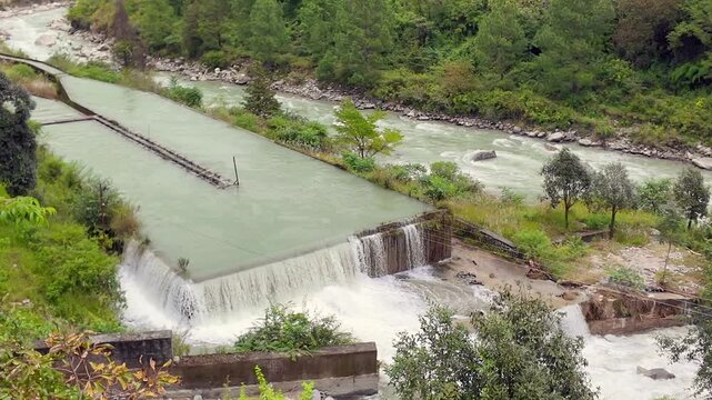 Water Overflowing Concrete Weir Beside Fast Mountain River in Forested Hills