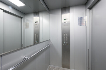 Elevator interior showcases stainless steel handrail, mirrored wall panel, metallic control panel with buttons, digital floor display, minimalist silver-grey design © evgeniykleymenov