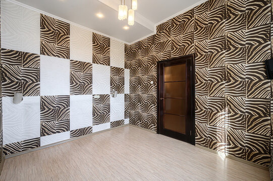 Room features zebra-print and white textured wall panels in checkerboard layout, dark wood door with glass inserts, light wood flooring, pendant lights, recessed ceiling lights