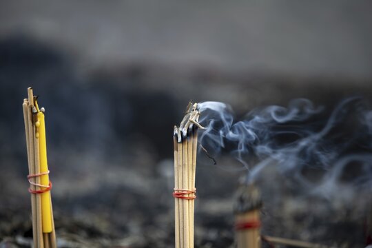 Fine smoke rises between the upright incense sticks and forms soft, swirling lines in the warm air. The bundles are carefully tied and depict a serene scene of traditional offerings such as those found in many temples and shrines, Wat Yai Chai Mongkon, Ayutthaya, Thailand