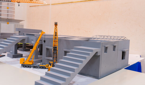 Architectural scale model of a precast concrete building under construction with miniature mobile cranes and stacked prefabricated wall panels