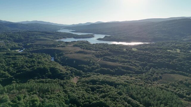 Aerial view flying over lush forest towards As Conchas reservoir