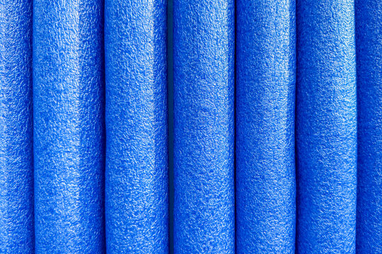 Close up of pool noodles standing vertically, rippled textured plastic surface and folds. Glossy blue foam swimming noodles lined up together, vibrant color, abstract background.